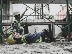 Injured construction worker with his coworker on his side calling for help.