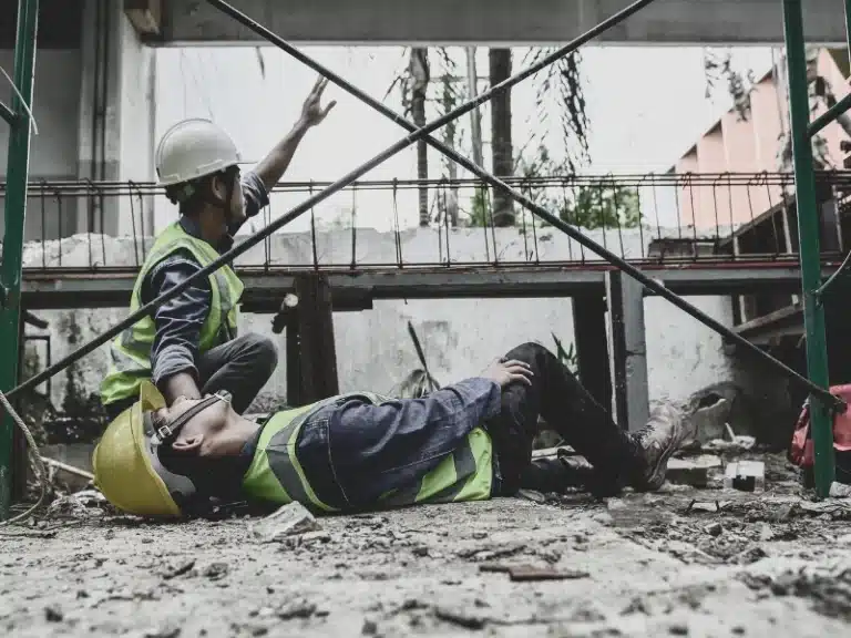 Injured construction worker with his coworker on his side calling for help.