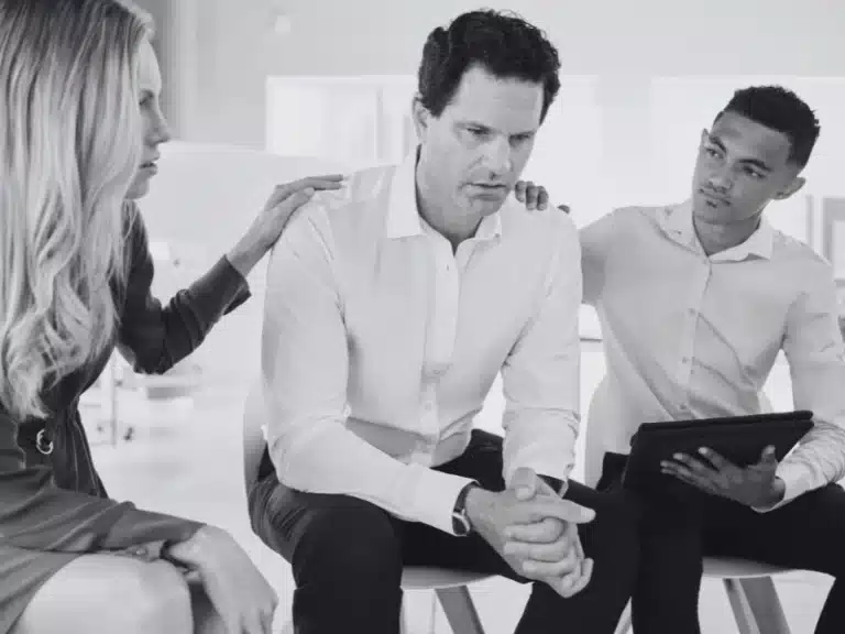 Distressed man being comforted by his team after an office argument.
