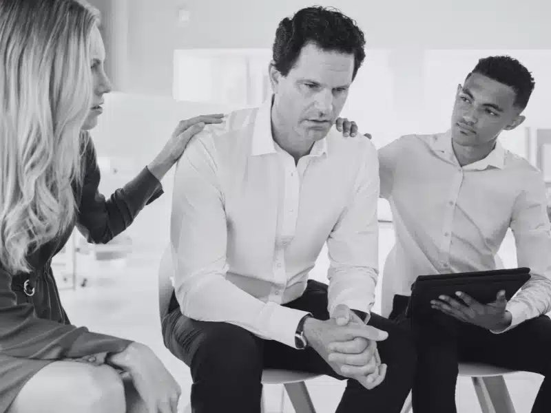 Distressed man being comforted by his team after an office argument.